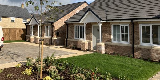 two newly built bungalows with light bricks and slate roofs. They have a small garden and driveway.