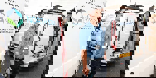 A repair worker stands between two branded vans from Ian Williams and North Star Housing. He is holding tools and wearing a blue uniform and lanyard. The vans display the logos and partnership between Ian Williams and North Star Housing.