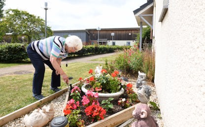 A woman tends to a flower bed surrounded by flowers and garden ornaments.