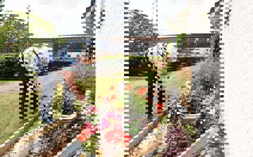 A woman tends to a flower bed surrounded by flowers and garden ornaments.