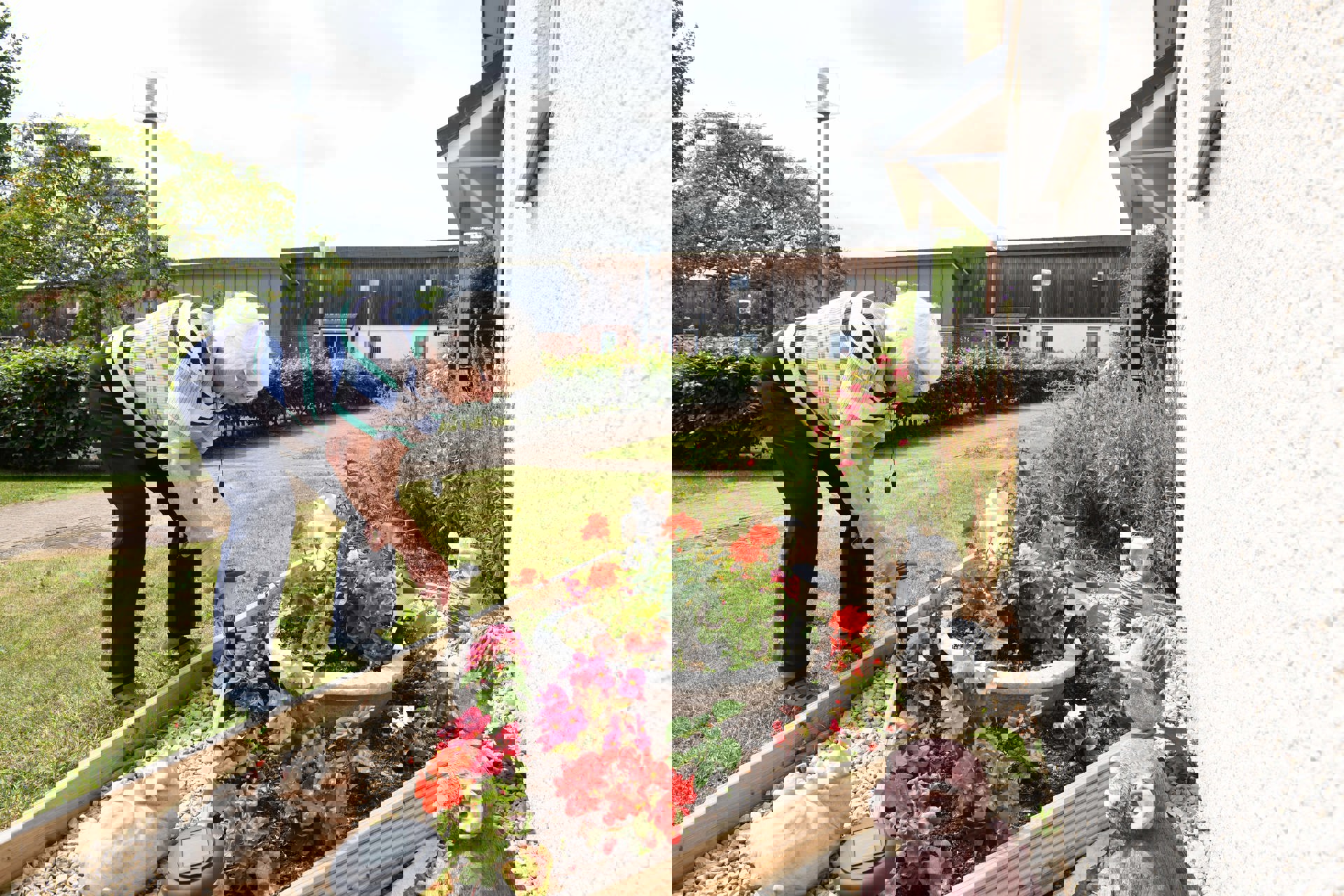 A woman tends to a flower bed surrounded by flowers and garden ornaments.