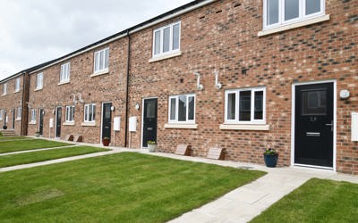 A row of terraced houses with light brick, black door and a lawn in front of the door.