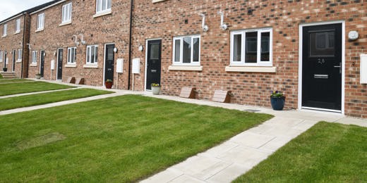 A row of terraced houses with light brick, black door and a lawn in front of the door.