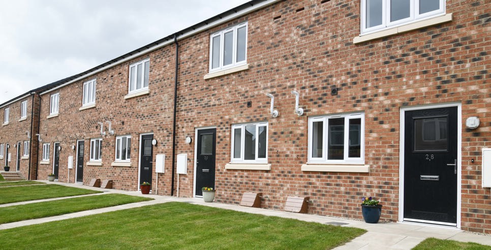 A row of terraced houses with light brick, black door and a lawn in front of the door.