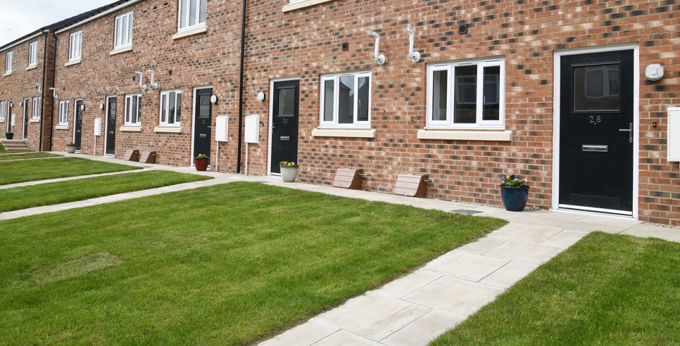 A row of terraced houses with light brick, black door and a lawn in front of the door.