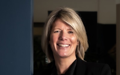 A woman in professional clothing smiles with her arms folded.