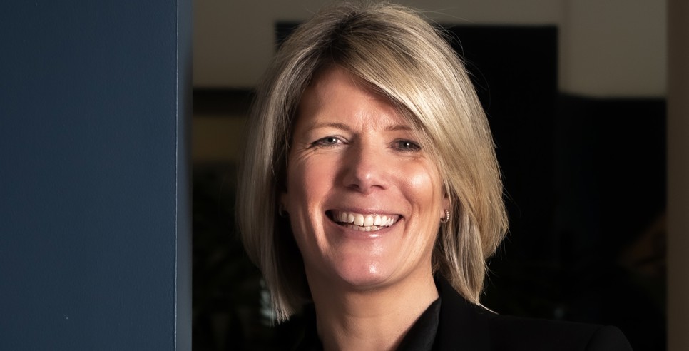 A woman in professional clothing smiles with her arms folded.